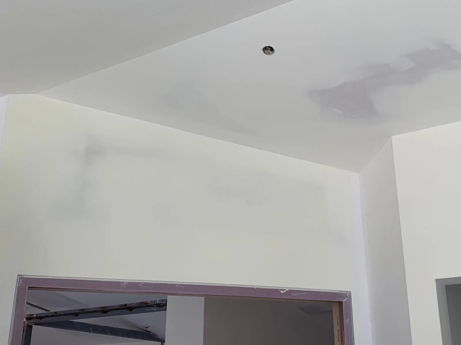 Angled ceiling plane meeting a wall above a wide cased opening, taped and coated.