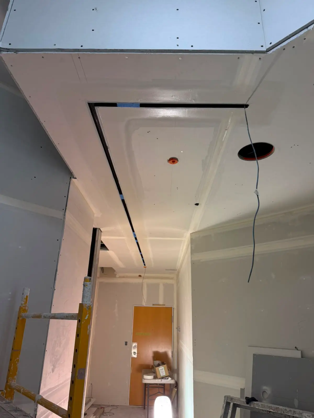 Corridor under construction with a boarded bulkhead and a black shadow-line reveal at the ceiling.